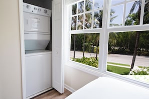 A laundry room with a built-in washer and dryer, a window with a view of palm trees and a street. - Blue House Getaway - 2BR 2.5BA Coastal Villa (Duck Key)