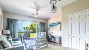 Une chambre avec un balcon, un ventilateur de plafond, une table à manger et un téléviseur fixé au mur.