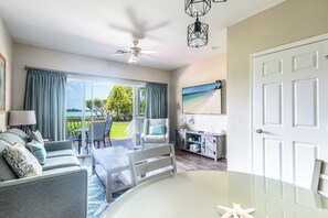 A room with a balcony, a ceiling fan, a dining table, and a TV mounted on the wall. - Blue House Getaway - 2BR 2.5BA Coastal Villa (Duck Key)