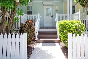 A front view of a house with a white picket fence, a front door, and a small porch with steps leading up to it. - Blue House Getaway - 2BR 2.5BA Coastal Villa (Duck Key)