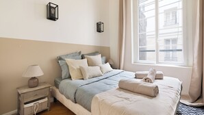 Ein ordentlich eingerichtetes Schlafzimmer mit Bett, Nachttisch, Lampe und einem Fenster mit Vorhängen.