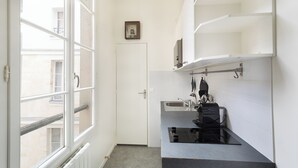Eine schmale Küche mit Fenster, weißen Schränken und einer schwarzen Arbeitsplatte.