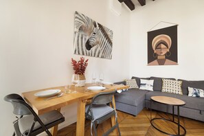Un coin repas avec une table en bois dressée pour deux personnes, un canapé gris et un tableau représentant une zèbre accroché au mur.