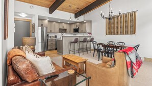 A modern living room with a leather sofa, a wooden coffee table, and a dining area with a red and black patterned tablecloth. - Mountain Views | Close to Slopes | Hot Tubs (steamboat springs)