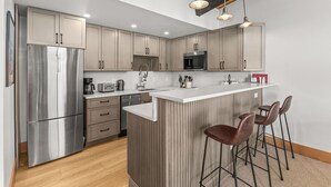 A modern kitchen with stainless steel appliances, wooden cabinets, and a central island with bar stools. - Mountain Views | Close to Slopes | Hot Tubs (steamboat springs)