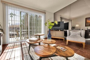A modern living room with a large TV, comfortable seating, and a balcony with a view. - Sunset Vista Retreat - A Ryson Property (Palm Springs)