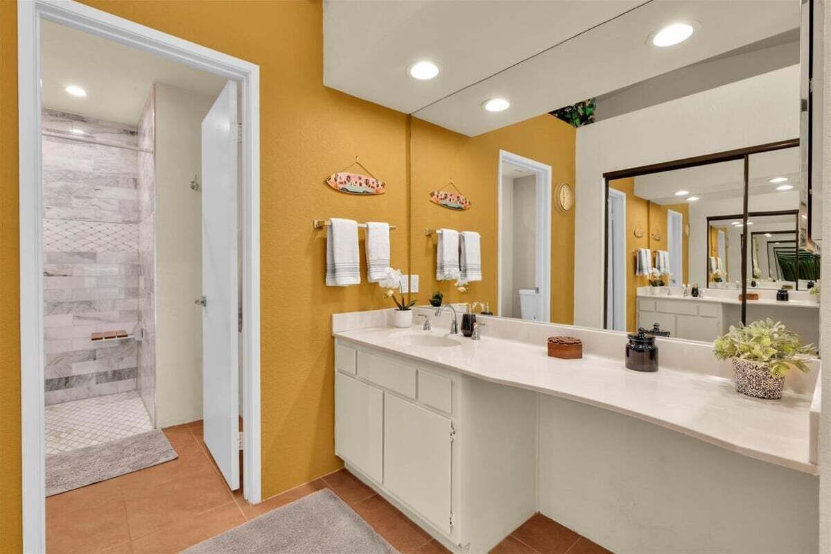 A bathroom with a white vanity, a large mirror, and two towel racks.