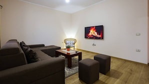 Una sala de estar con un sofá, otomanas, una mesa de centro, un televisor que muestra una chimenea y una lámpara.