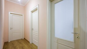 Un pasillo con tres puertas blancas, suelo de madera y paredes rosadas claras.