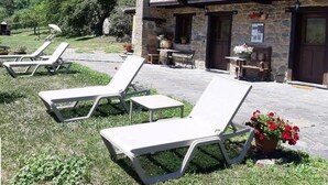 Un bâtiment en pierre doté d’un patio aménagé avec des chaises longues et des plantes en pot.
