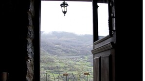 Une entrée avec un sol en pierre qui mène à un point de vue sur un paysage rural, avec une clôture et une lanterne suspendue.