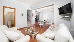 Un soggiorno moderno con un tavolino in vetro, divani bianchi, un'area pranzo con tavolo in vetro e una TV a parete.