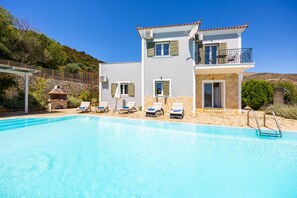 Ein zweistöckiges Haus mit Swimmingpool, Sitzgelegenheiten im Freien und einer Steinmauer.