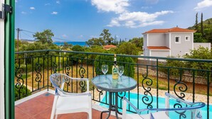 A balcony with a glass table and chairs, a pool, and a view of the sea and buildings. - a beautiful holiday home located in Katelios, Kefalonia (Katelios)