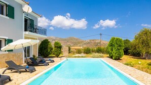 A swimming pool with lounge chairs and umbrellas, surrounded by greenery and mountains. - a beautiful holiday home located in Katelios, Kefalonia (Katelios)