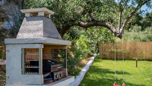 A small, white outdoor grill with a chimney, surrounded by a grassy yard and a wooden fence. - peaceful Kefalonia villa with private pool (Spartia)