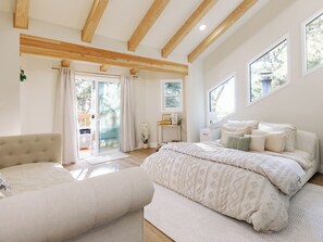 Ein Schlafzimmer mit einem großen Bett, einem kleinen Sofa, einem Schreibtisch mit Stuhl und einer Glastür zum Außenbereich.