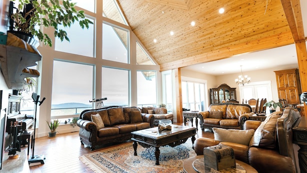 A spacious living room with high ceilings and large windows, furnished with leather sofas and a grand piano. - Blue Horizon Mountain Retreat B&B  (Shawnigan Lake)