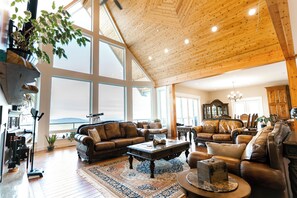 A spacious living room with high ceilings and large windows, furnished with leather sofas and a grand piano. - Blue Horizon Mountain Retreat B&B  (Shawnigan Lake)