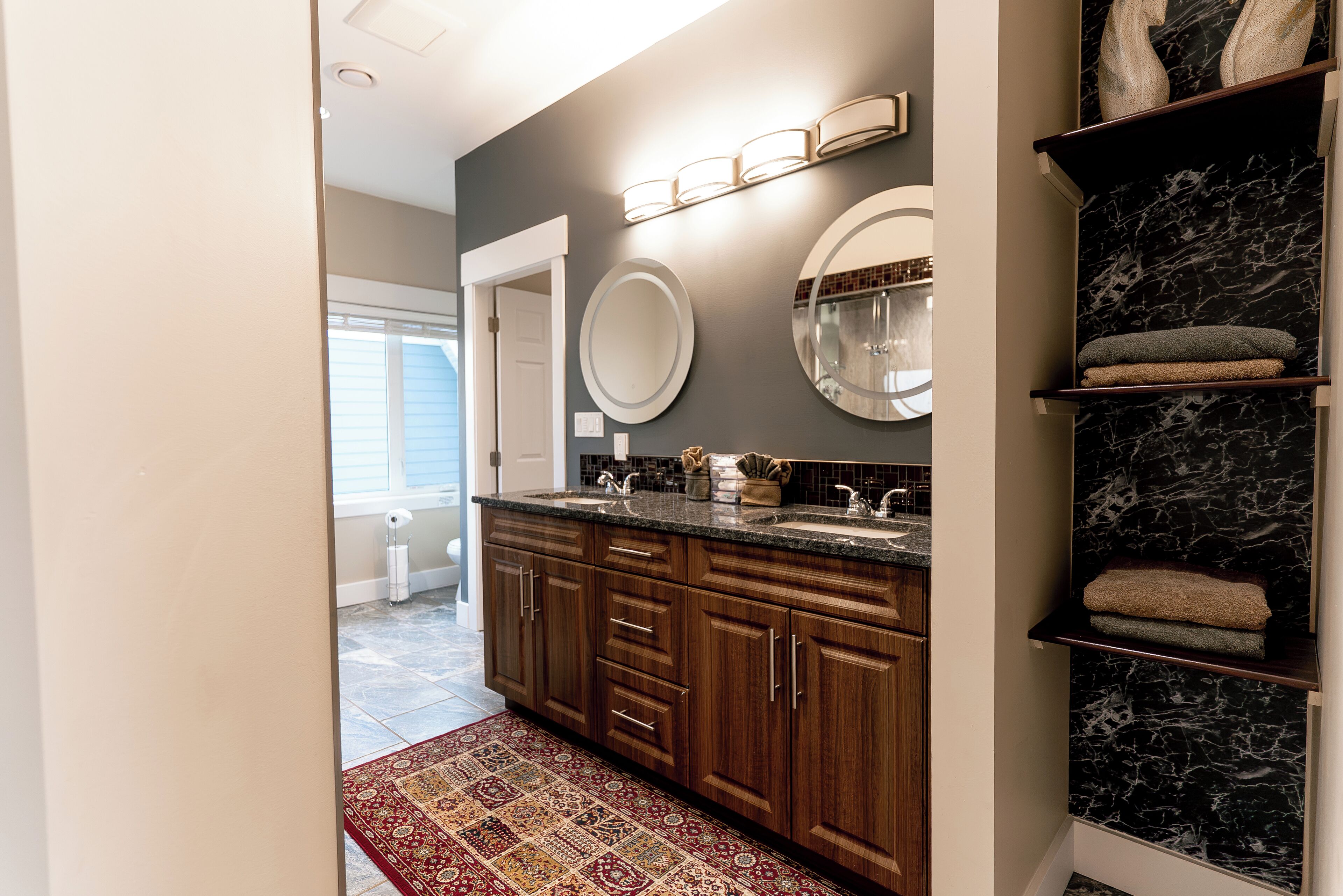A modern bathroom with a marble vanity, dual sinks, and a built-in shelf with towels.