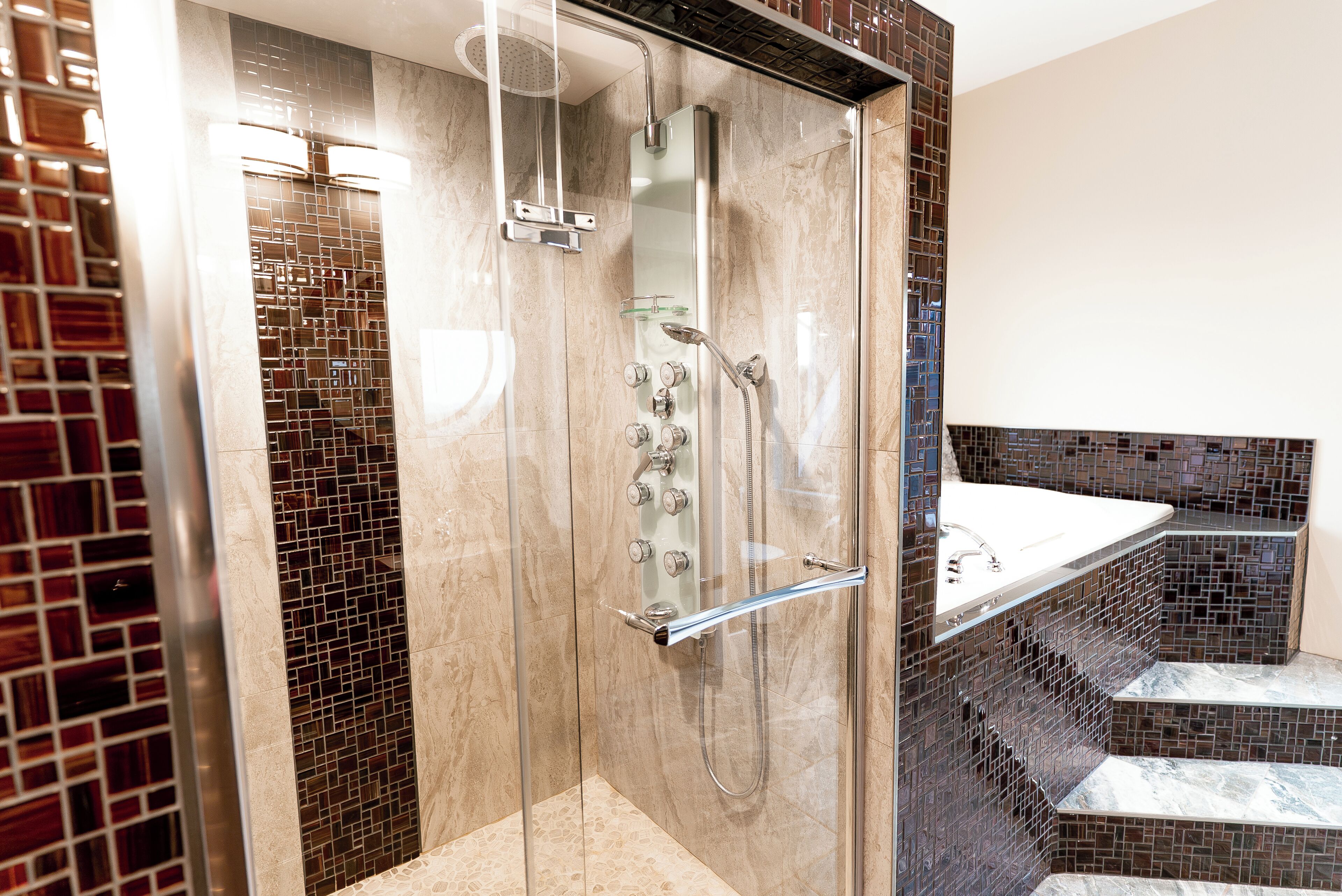 A modern bathroom with a glass-enclosed shower, a marble-tiled wall, and a built-in sink with a glass ledge.