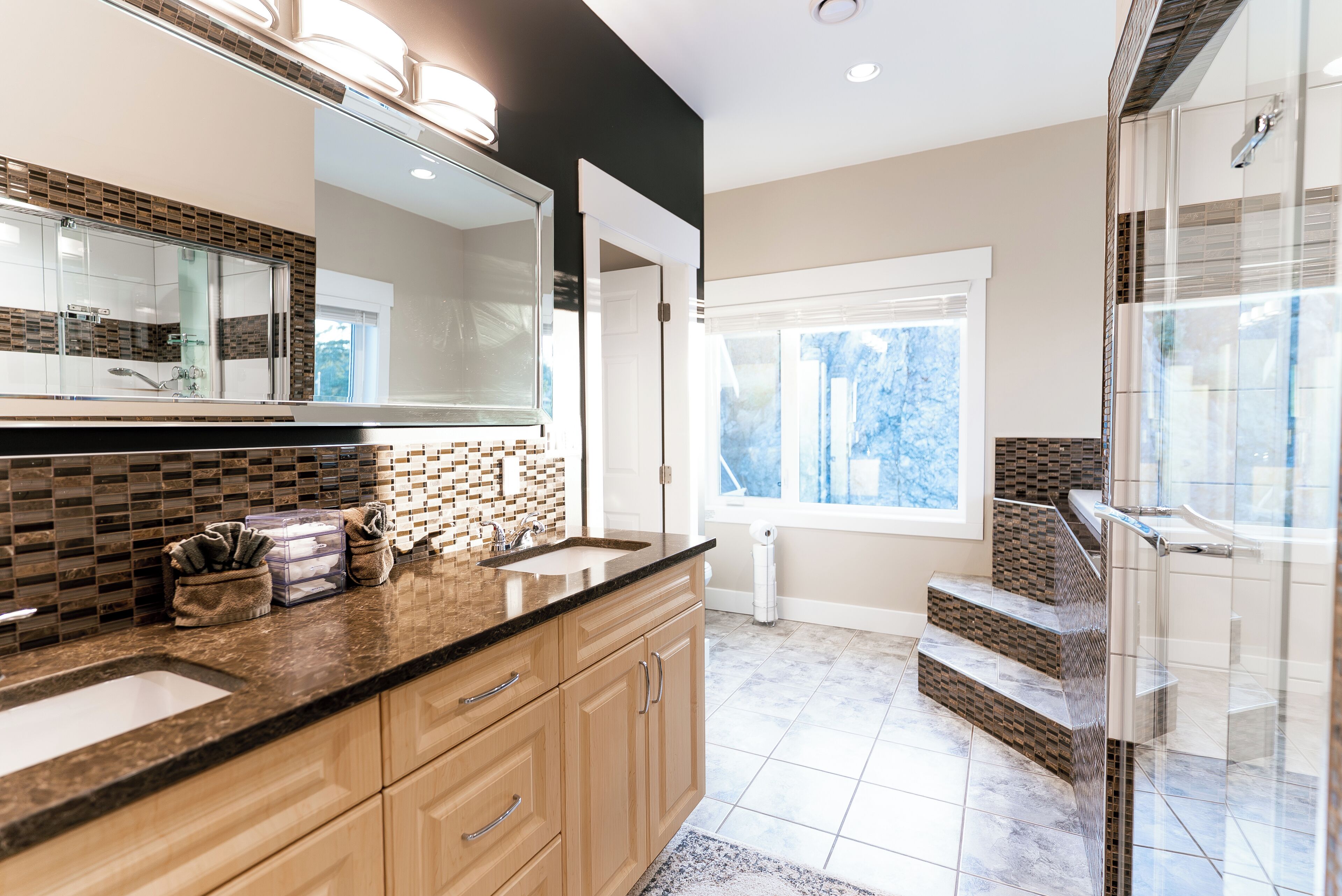 A modern bathroom with a large mirror, two sinks, and a shower area.