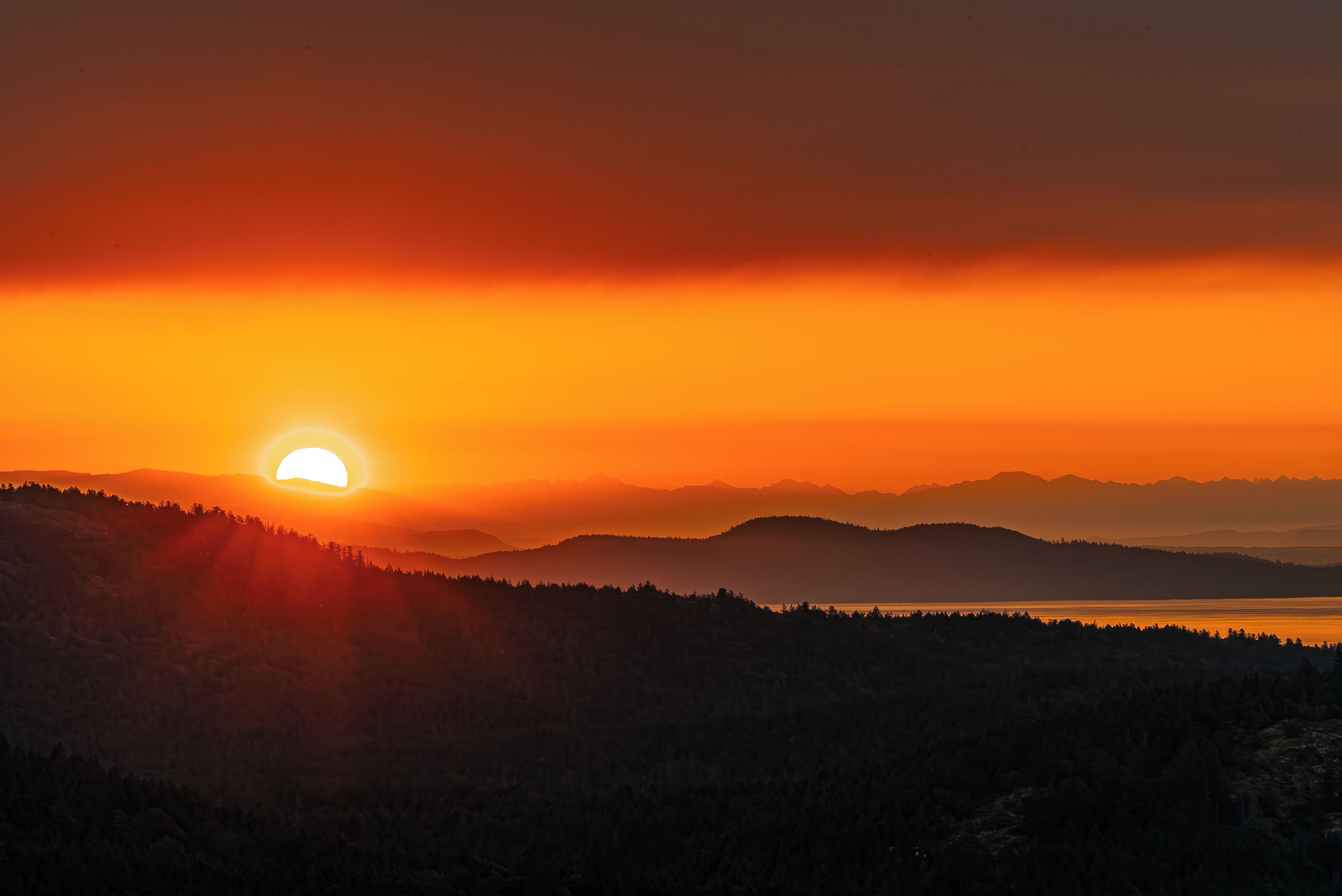 Auringonlasku vuoristomaisemassa, jossa etualalla on vesistö.