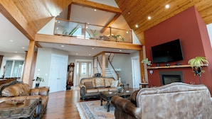 A spacious living area with a high ceiling, wooden beams, a staircase, and a mounted television. - Blue Horizon Mountain Retreat B&B  (Shawnigan Lake)