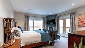 A spacious bedroom with a large bed, a TV mounted on the wall, and a view of the outdoors through the windows. - Blue Horizon Mountain Retreat B&B  (Shawnigan Lake)