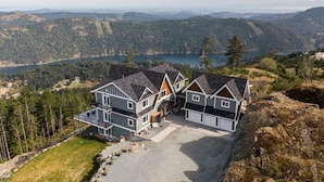 A modern two-story house with a large driveway and a view of a lake and forested hills. - Blue Horizon Mountain Retreat B&B  (Shawnigan Lake)
