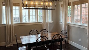 Een eetruimte met een rechthoekige tafel, zes stoelen, een kroonluchter en grote ramen voorzien van gordijnen.