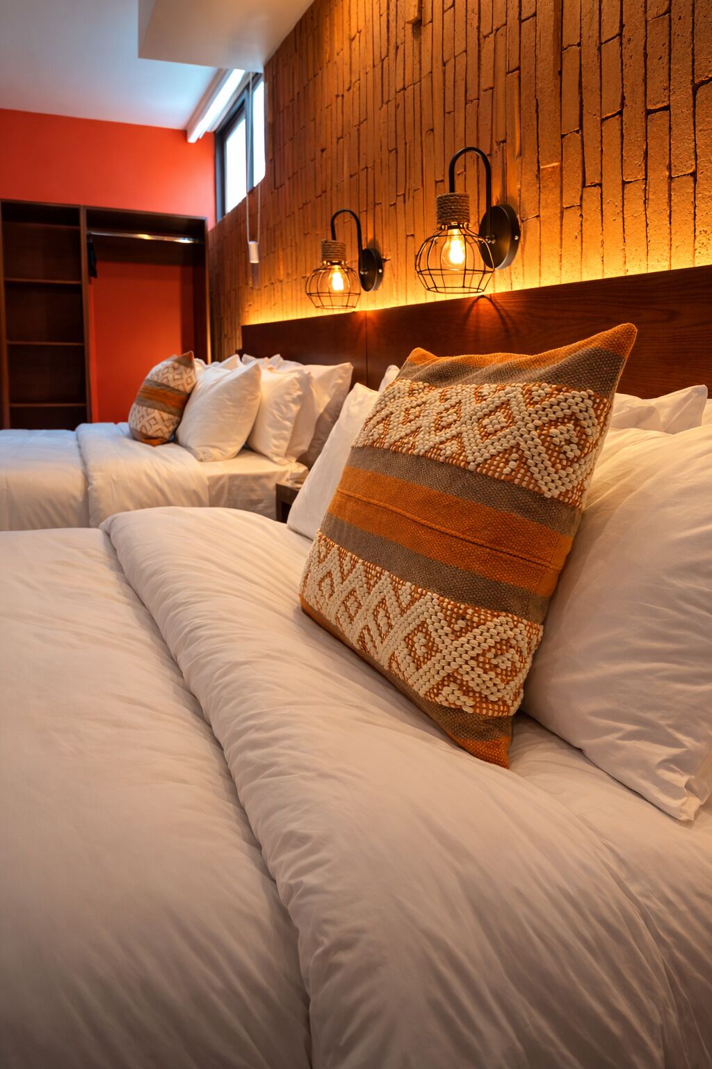 A hotel room with a brick-patterned wall, two beds with white bedding, and two wall-mounted light fixtures.
