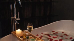 A bathtub with rose petals, candles, and a tray with bottles and a glass of wine. - Hotel boutique Casa Gopar (Ocotlán de Morelos)
