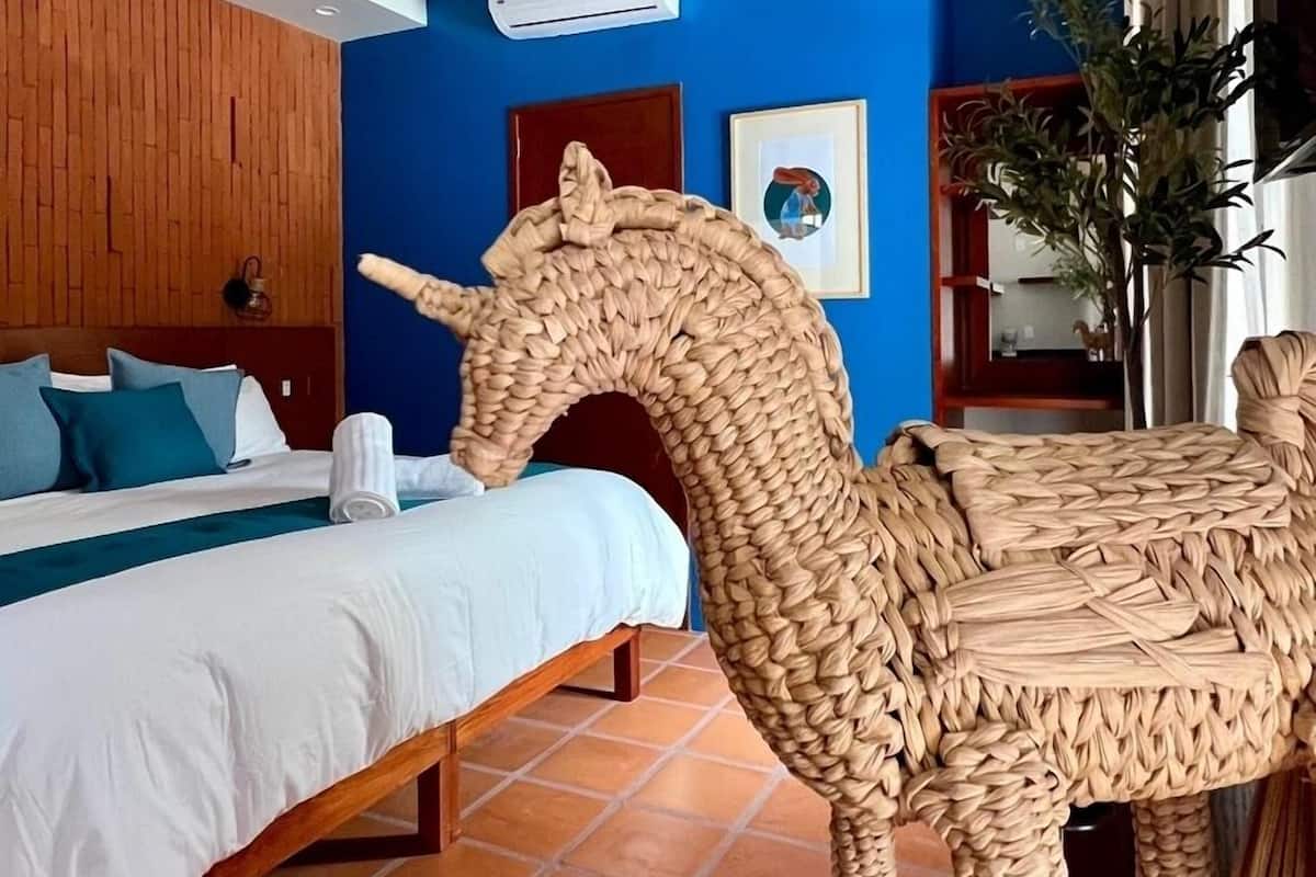 Una camera d'albergo con un letto, una scultura di cavallo in fibra naturale, una parete blu e una finestra con tende.