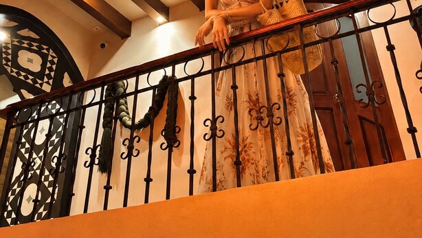 A woman on a balcony with a decorative chandelier, a wrought iron railing, and a patterned wall. - Hotel boutique Casa Gopar (Ocotlán de Morelos)