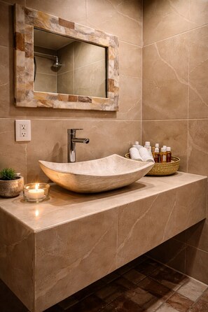 A bathroom with a large vessel sink, a mirror with a stone frame, a towel rack, and a candle. - Hotel boutique Casa Gopar (Ocotlán de Morelos)
