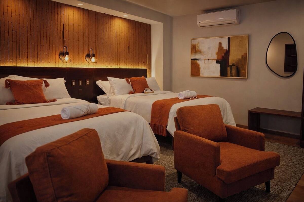 Una camera d'albergo con due letti, una testiera in legno, uno specchio grande e una panca.