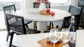 A round dining table with a white tablecloth, surrounded by black mesh chairs. A vase with red foliage is placed on the table, and there are plates with apples and a bottle of wine. - Luxury Ranch Near Palo Pinto Park with 10 Beds (Strawn)