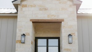A stone building with a central entrance, two wall-mounted lanterns, and a set of steps leading up to the door. - Luxury Ranch Near Palo Pinto Park with 10 Beds (Strawn)