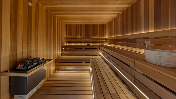 Una sauna con bancos de madera, un banco con un recipiente y un calentador de pared.