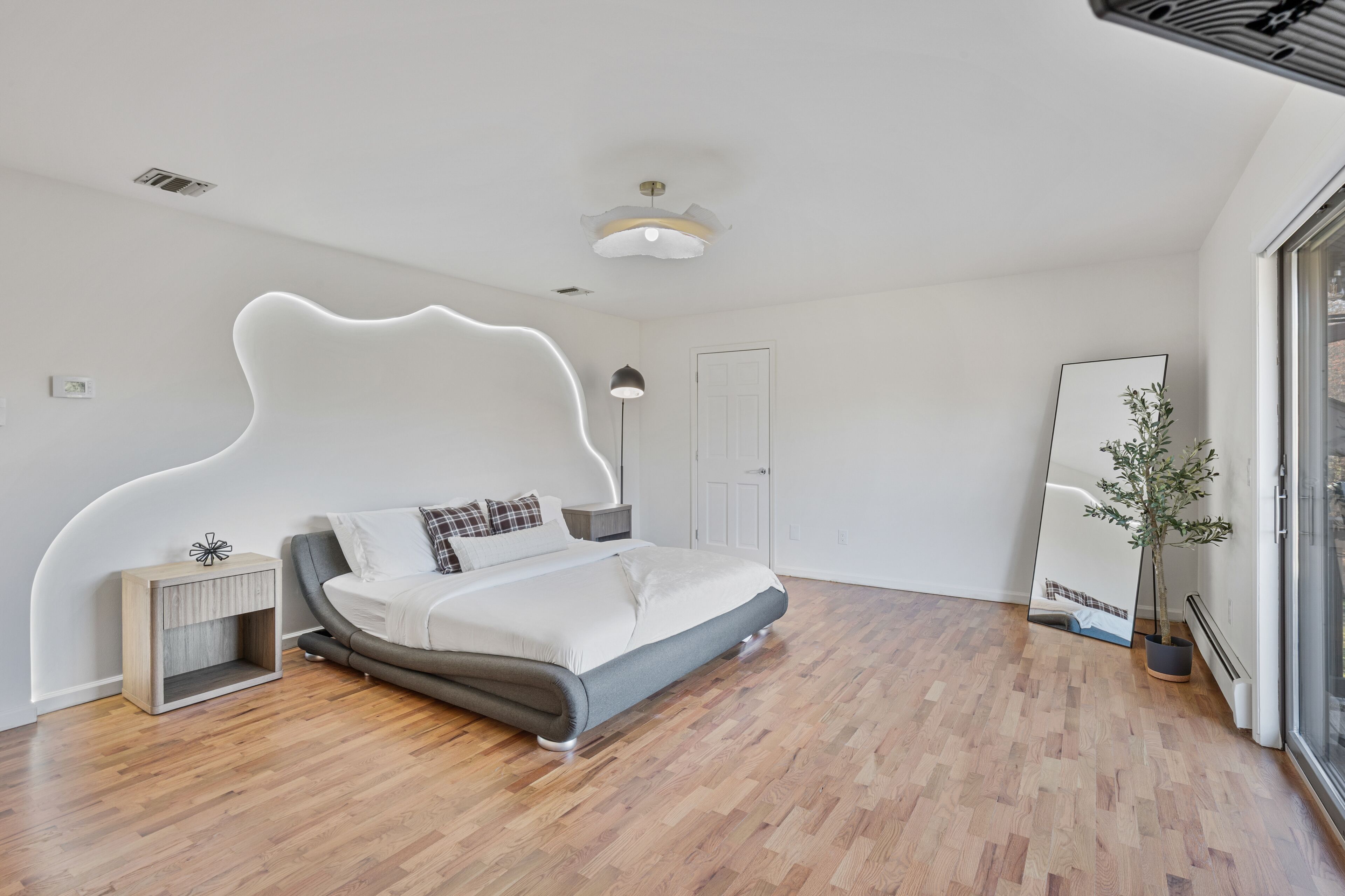 Une chambre à coucher moderne avec un lit, une table de chevet et un grand miroir.