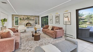 Una sala de estar moderna con chimenea de piedra, asientos cómodos y ventanas grandes con vistas al exterior.