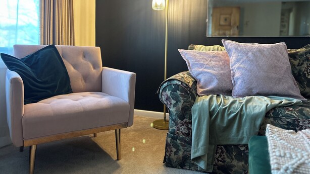 A living room with a light-colored armchair, a floral-patterned sofa, and a floor lamp. - Bobbi's on the Hill (Waynesville)