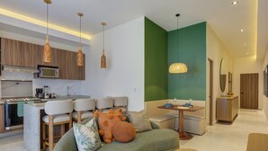 A modern kitchen with a built-in microwave, a stove, and a coffee maker. There is a dining area with a table and chairs, and a living room with a sofa and a coffee table. - Rooftop Pool & Ocean Views Malecón, 5 de Diciembre (Puerto Vallarta)