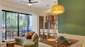 A modern living room with a green sofa, a dining table set with plates and glasses, and a large window with a view of greenery. - Rooftop Pool & Ocean Views Malecón, 5 de Diciembre (Puerto Vallarta)