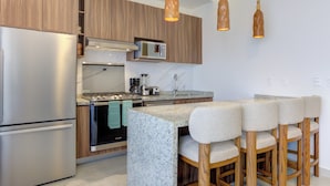 A modern kitchen with wooden cabinets, stainless steel appliances, a granite countertop, and bar stools. - Rooftop Pool & Ocean Views Malecón, 5 de Diciembre (Puerto Vallarta)
