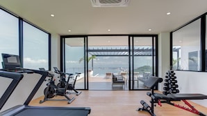 Een fitnessruimte met loopbanden, hometrainers en gewichtbanken, met grote ramen en uitzicht op de stad.