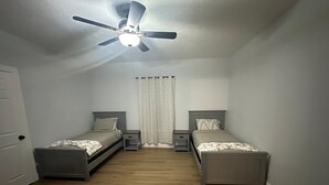 Une chambre avec deux lits simples, un ventilateur de plafond et une fenêtre avec des rideaux.