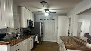 Une cuisine moderne avec des meubles blancs, un four à micro-ondes, un réfrigérateur et un ventilateur de plafond.