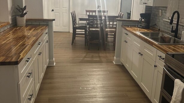 Une cuisine moderne avec des plans de travail en bois, des armoires blanches, un coin repas avec une table et des chaises, et un ventilateur de plafond.